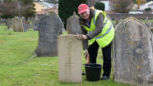 An Eyes On, Hands On volunteer scrubs a headstone.