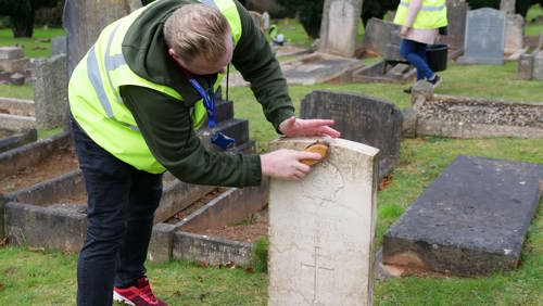 An Eyes On, Hands On volunteer scrubs a headstone.